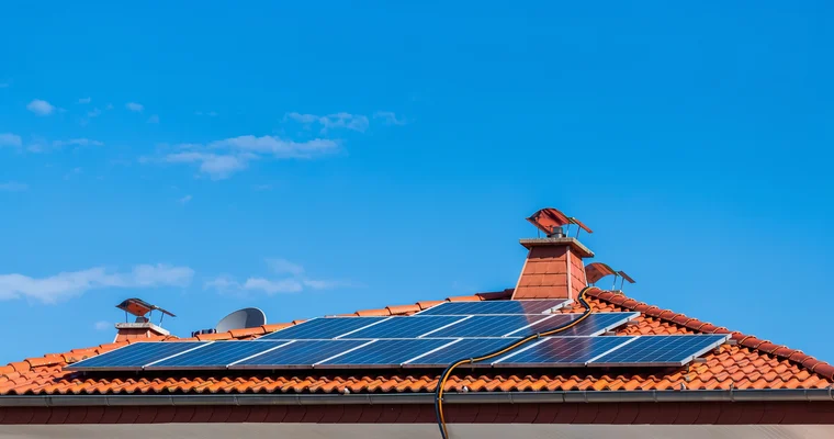 Placas solares instaladas en un tejado de teja bajo un cielo azul