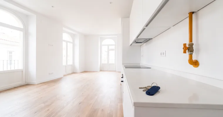 Cocina de una vivienda nueva y vacía con la tubería y la llave de paso del gas en la pared y las llaves sobre la encimera